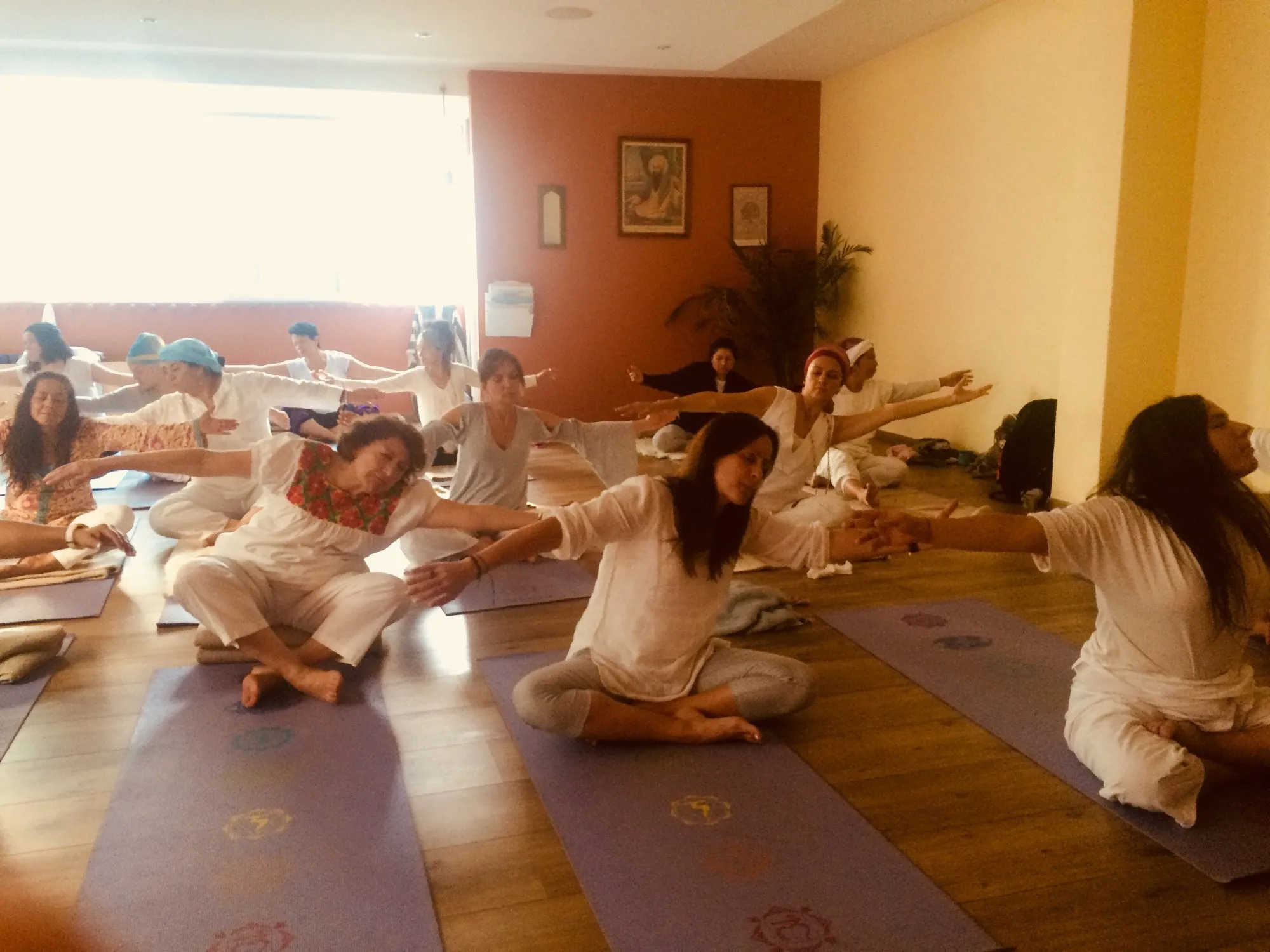 Shakti Dance practitioners in white performing seated movement with extended arms on chakra-patterned mats