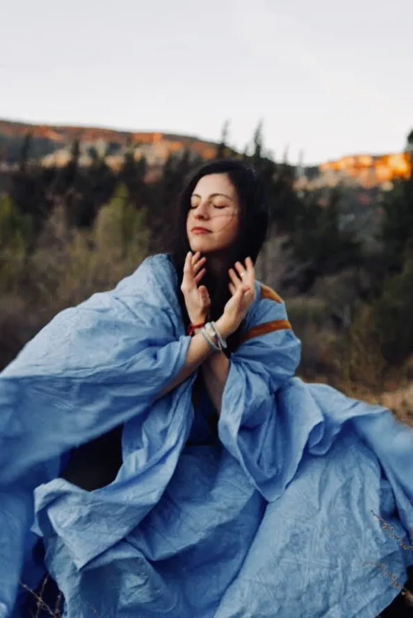 Silvia La wrapped in flowing blue fabric in a meditative pose outdoors